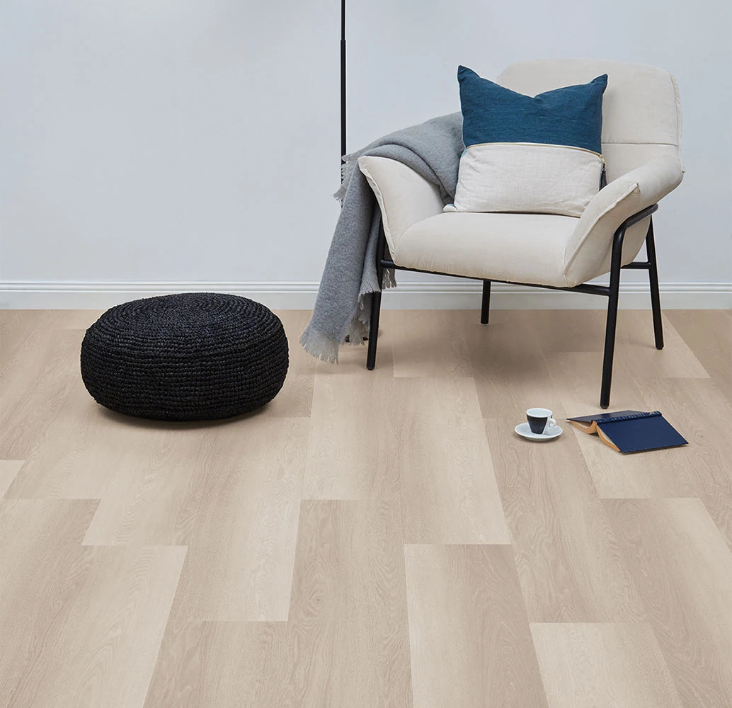 Smoked Oak Vinyl Plank Nordic Beech in a light-filled sitting room with a cream armchair, woven pouf and blue cushion