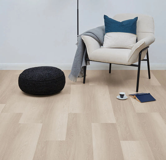 Smoked Oak Vinyl Plank Nordic Beech in a light-filled sitting room with a cream armchair, woven pouf and blue cushion