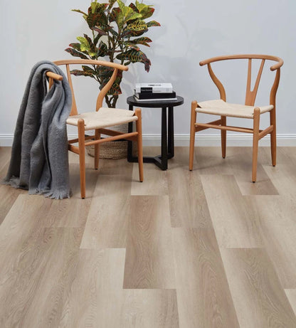 Smoked Oak Vinyl Plank Rivermalt in a Scandi-style sitting area with wishbone chairs, a black side table and a grey throw